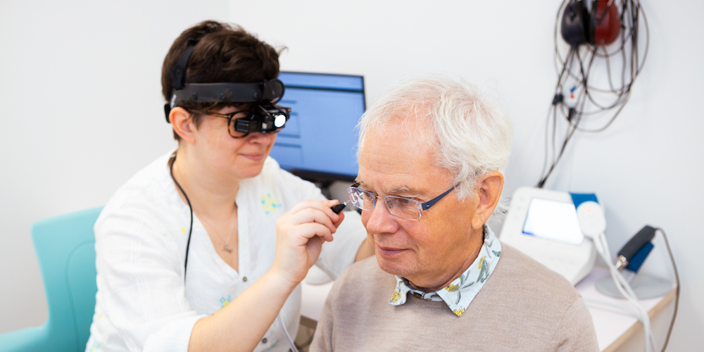 Male patient having ear wax removal performed by female audiologist.