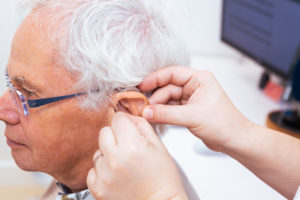 An audiologist is putting a hearing aid into a patient's ear.