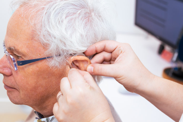 An audiologist is putting a hearing aid into a patient's ear.