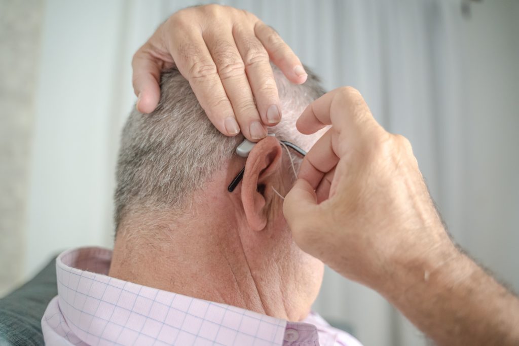 The view is of the back and right side of a man's head and he is putting a receiver-in-canal hearing aid into his right ear.