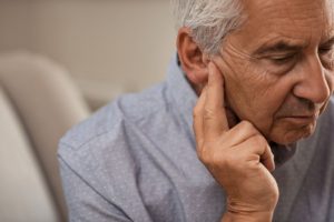 An older man with tinnitus is rubbing his ear to help relieve his tinnitus symptoms.